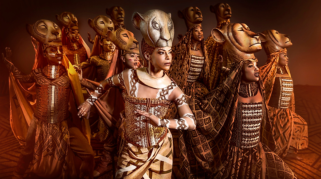Disneys DER KÖNIG DER LÖWEN: Darsteller:innen in Kostümen auf der Bühne vor afrikanischer Kulisse.