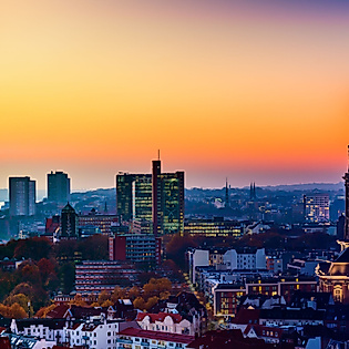 Panorama von Hamburg bei Sonnenuntergang mit beleuchtetem Michel-Turm und Hafen im Hintergrund.