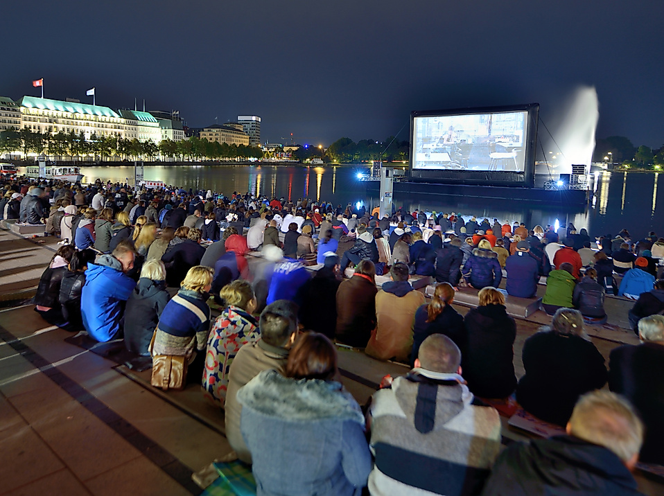 Zuschauer:innen beim Binnenalster-Filmfest in Hamburg vor einer Leinwand am Wasser bei Nacht