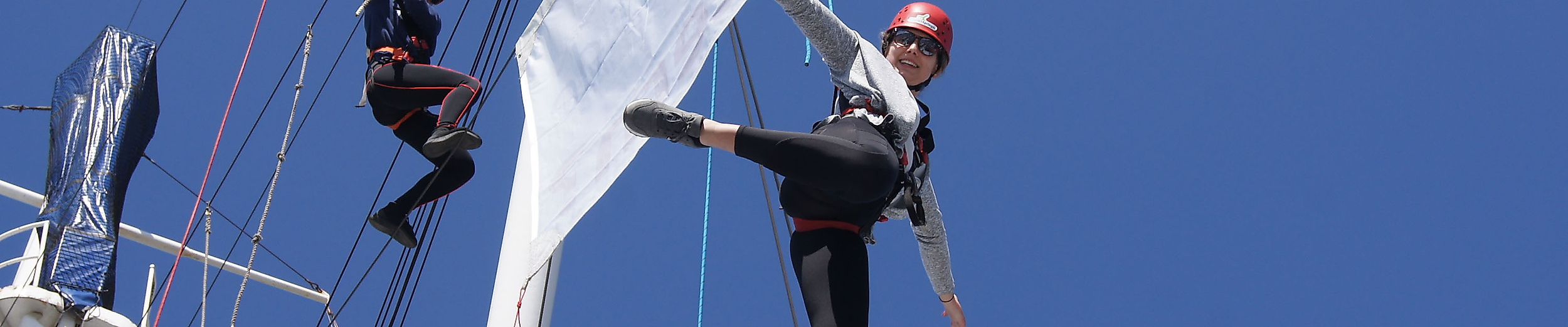 Zwei gesicherte Kletternde an einem Schiffsmast der Cap San Diego vor blauem Himmel