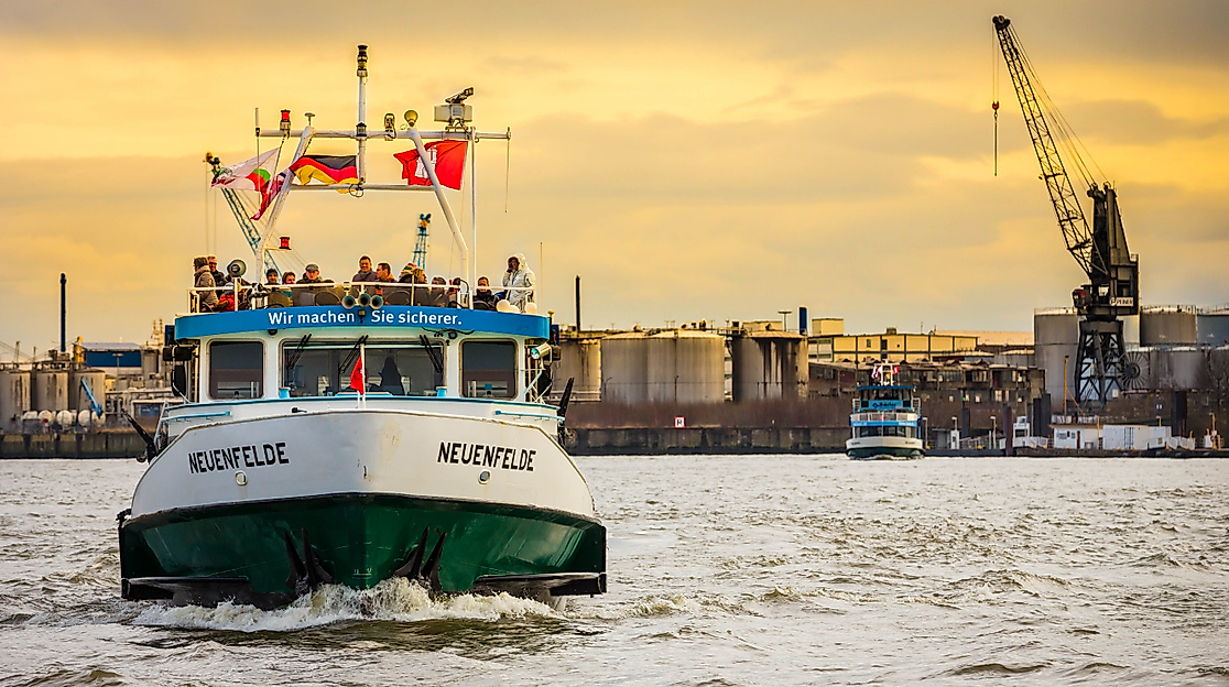 Barkasse im Hamburger Hafen bei Sonnenaufgang mit Signalflaggen und Hafenanlagen im Hintergrund