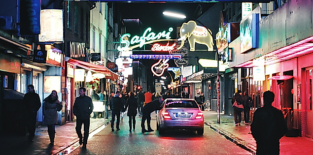 Nächtliche Szene auf der Großen Freiheit mit bunten Leuchtreklamen und Passant:innen vor Clubs wie dem Dollhouse.