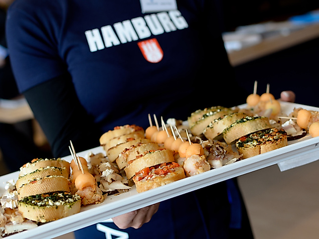 Person mit Hamburg-Shirt serviert Platte mit Fischbrötchen und Fingerfood-Häppchen