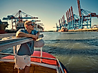 Mann auf Barkasse im Hamburger Hafen bei Sonnenschein mit Blick auf Containerterminals im Sommer