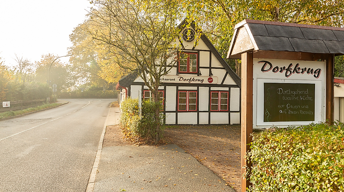 Reetgedecktes Fachwerkhaus Dorfkrug mit Restaurant „Eingang“-Schild in herbstlicher Landschaft bei Sonnenlicht in Hamburg