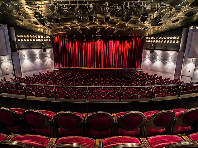 Blick in den Theatersaal des Winterhuder Fährhauses mit roten Sitzreihen und geschlossener Bühne
