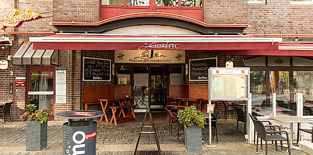 Außenansicht des Lava-Hauses in Hamburg-Bergedorf mit Gastronomie, roter Markise und Bestuhlung auf dem Vorplatz.