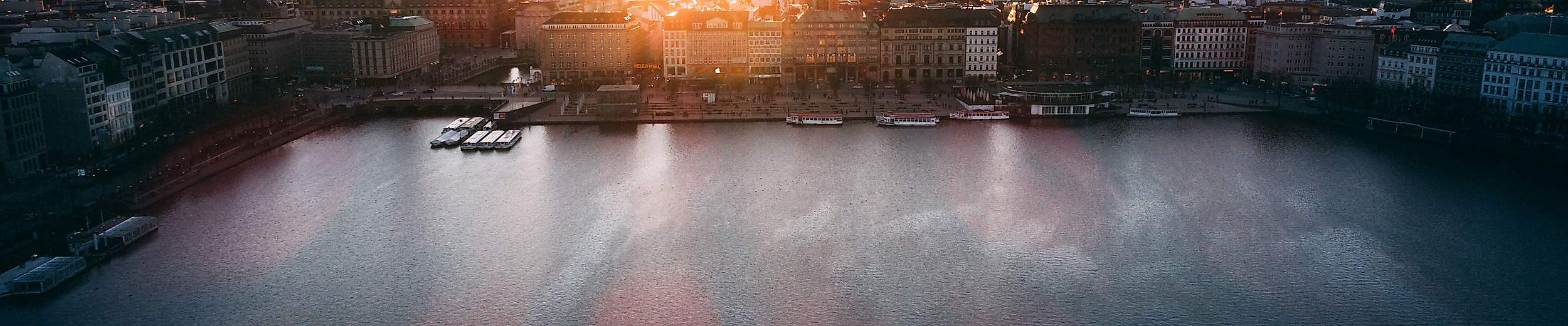 Panoramablick auf die Binnenalster bei Sonnenuntergang mit Kirchtürmen der Hamburger Altstadt.