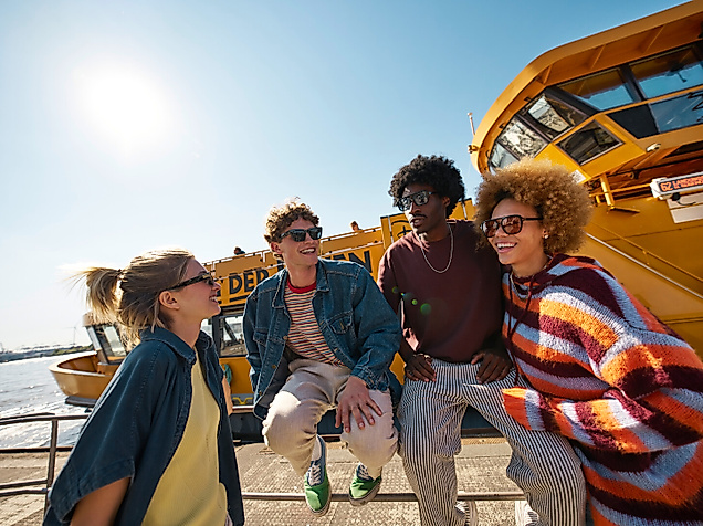 Four people wearing sunglasses in front of a harbour ferry in Hamburg