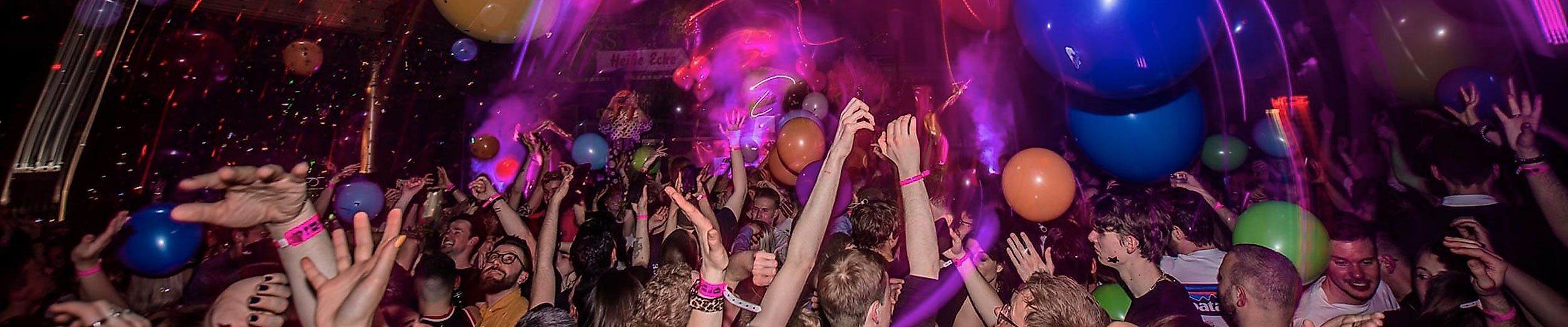 Bunte Party mit Luftballons, Lichteffekten und jubelndem Publikum in ausgelassener Queer-Bar-Atmosphäre