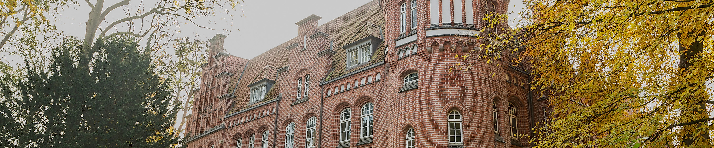 Backsteinfassade des Bergedorfer Schlosses in Hamburg, umgeben von herbstlichen Bäumen und Weg im Vordergrund
