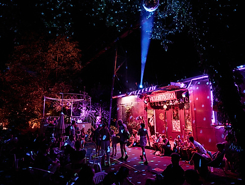 Party in front of the Migrantpolitan. Guests move around in pink light beneath a disco ball.