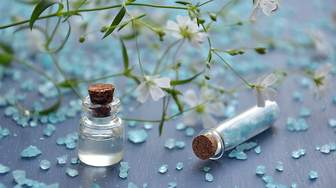 Kleine Glasfläschchen mit Badezusatz und blauen Kristallen auf dekorativer Wellness-Oberfläche