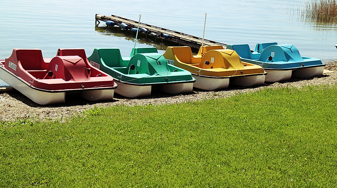 Bunte Tretboote am Ufer nebeneinander aufgereiht, bereit zur Ausleihe an einem sonnigen See
