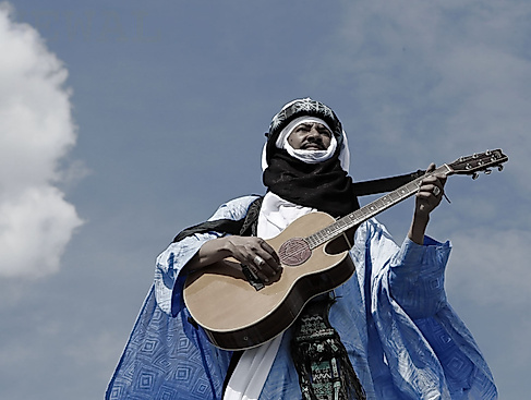Alhousseini Anivolla is standing on a rooftop with a guitar. The sky can be seen in the background.