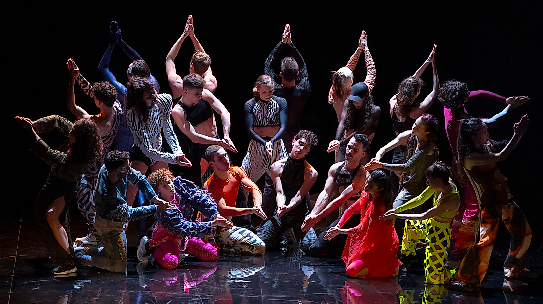 Excerpt from Marco da Silva Ferreira’s “A Folia.” A group of dancers stands in a semicircle wearing colorful costumes.