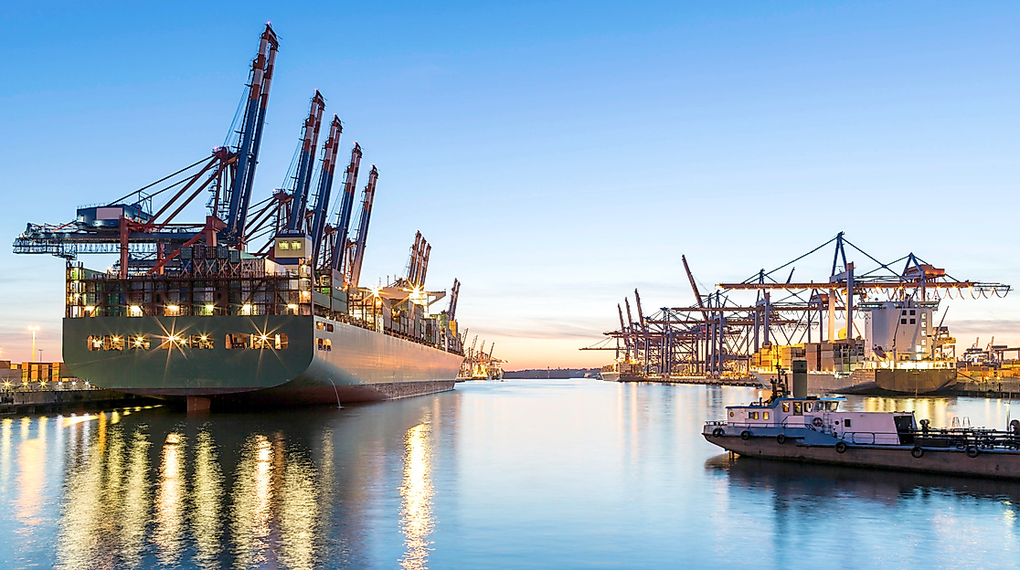 Beleuchtetes Containerschiff im Hamburger Hafen bei Abendstimmung mit Kränen und Wasserreflexion