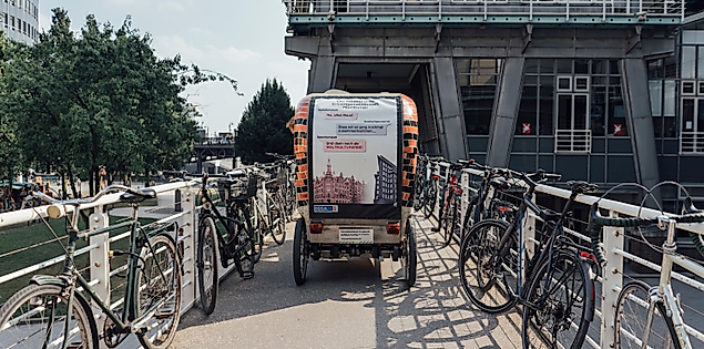 Rikscha auf Brücke zwischen abgestellten Fahrrädern vor modernem Gebäude in Hamburg