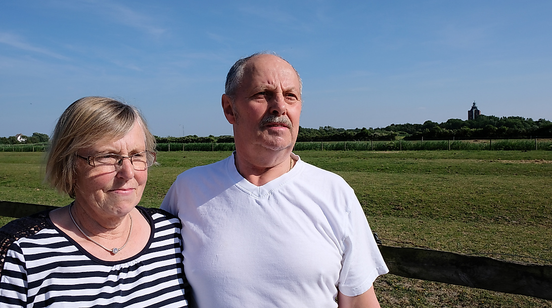 Älteres Paar vor grüner Wiese auf der Hamburger Insel Neuwerk mit Blick auf den historischen Leuchttur