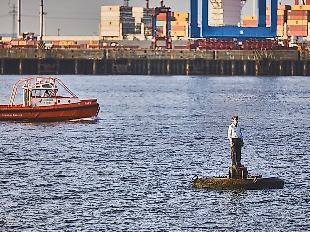 Skulptur „Die Auswanderer“ auf Boje in der Elbe vor Containerschiffen und Ausflugsboot