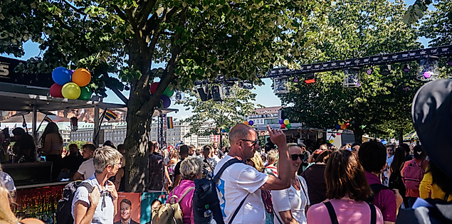 Menschen feiern beim CSD Hamburg unter Bäumen mit Regenbogenfarben, Schildern und bunter Pride-Stimmung