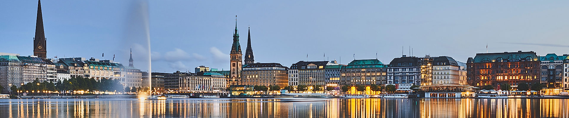 Beleuchtete Hamburger Innenstadt spiegelt sich abends in der ruhigen Binnenalster mit Blick auf Alsterfontäne