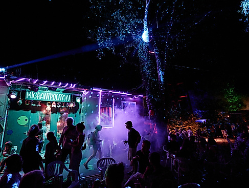 Migrantpolitan at night, with a party atmosphere, fog, and colorful lights