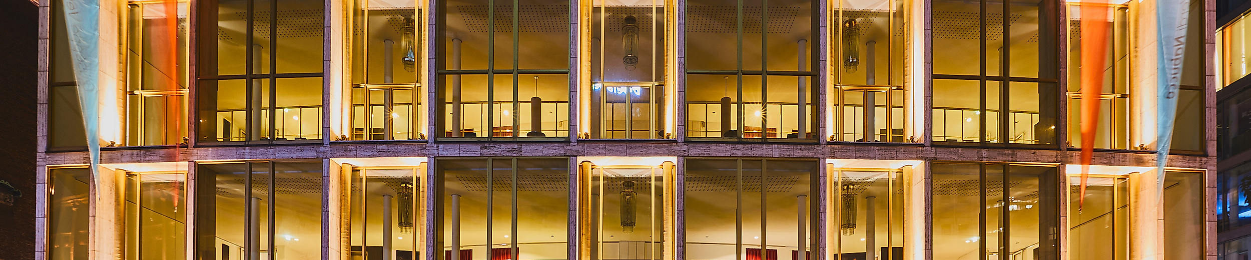 Frontansicht der hell erleuchteten Hamburgischen Staatsoper bei Nacht mit verglastem Eingangsbereich.