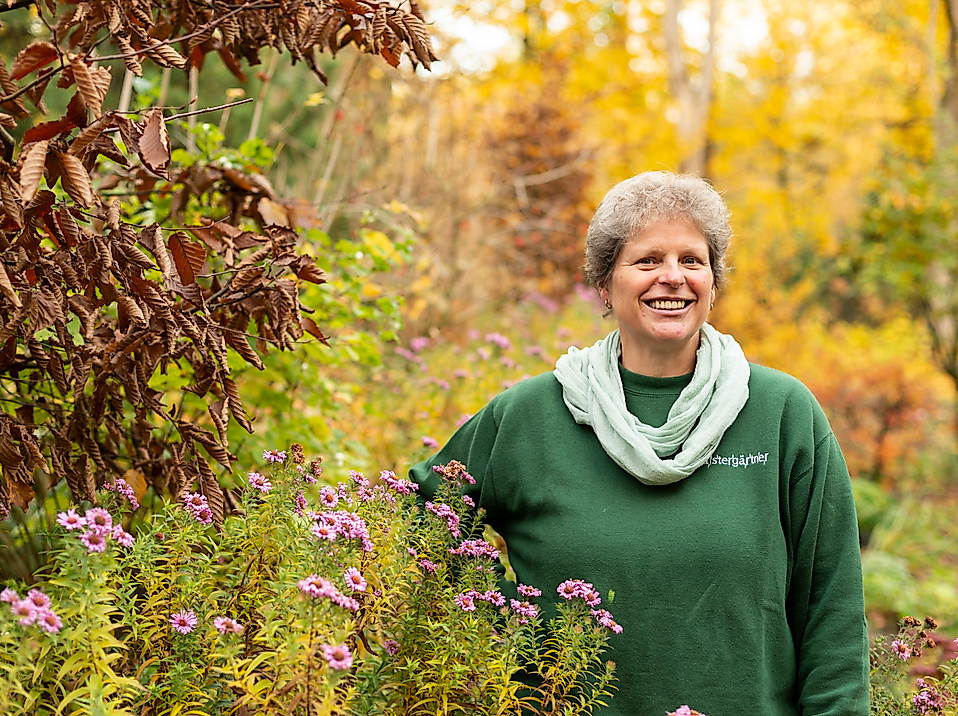 Lächelnde Person im herbstlich blühenden Garten in Hamburg, umgeben von buntem Laub und Wildstauden