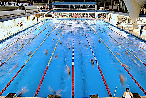Großes Schwimmbecken mit mehreren Bahnen, in dem zahlreiche Personen gleichzeitig trainieren