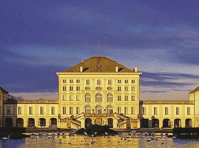 Schloss Nymphenburg in München bei Abenddämmerung mit Spiegelung im Wasser des Schlosskanals.