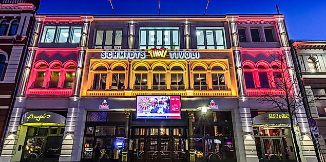 Beleuchtete Fassade von Schmidts Tivoli auf der Reeperbahn bei Abenddämmerung mit Besucher:innen vor dem Eingang