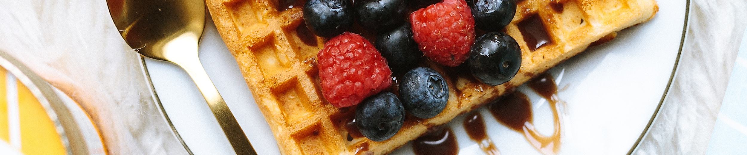 Waffel mit frischen Beeren und Schokosoße auf Teller, serviert mit Eiscreme und goldfarbenem Löffel