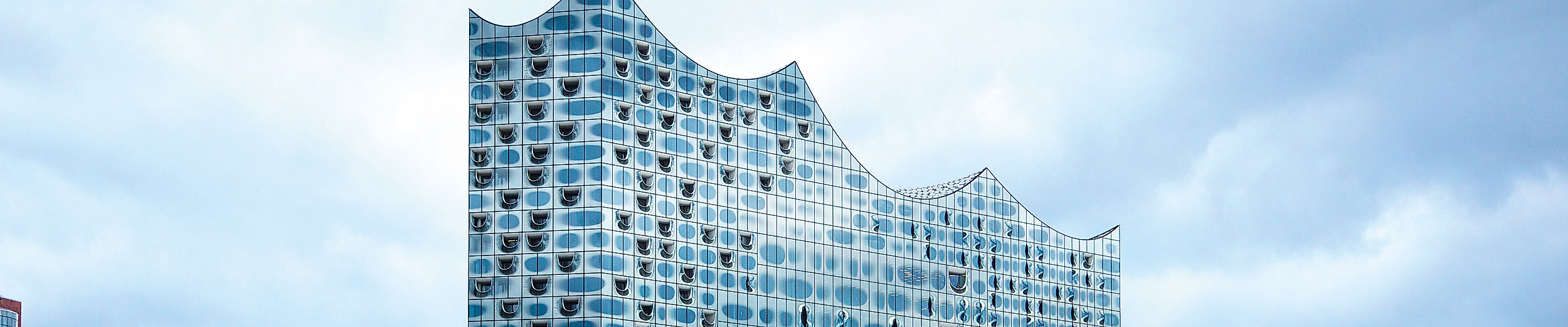 Moderne Glasfassade der Elbphilharmonie in Hamburg mit wolkigem Himmel, Wahrzeichen der Musikstadt.