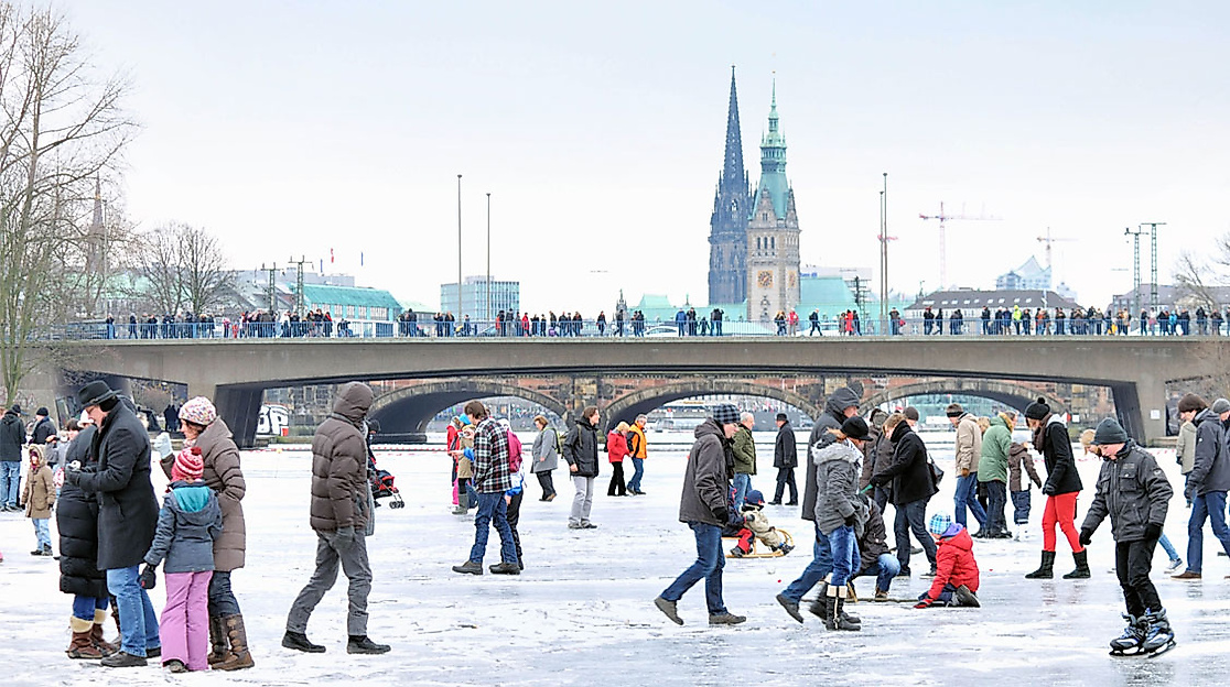 Menschenmenge auf zugefrorener Binnenalster in Hamburg mit Lombardsbrücke und Kirchtürmen im Hintergrund