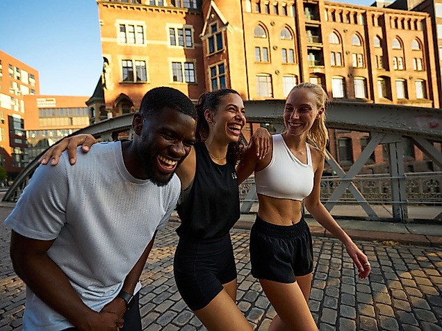 Drei junge Menschen in Sportkleidung lachen gemeinsam beim Spaziergang durch die Hamburger Speicherstadt.