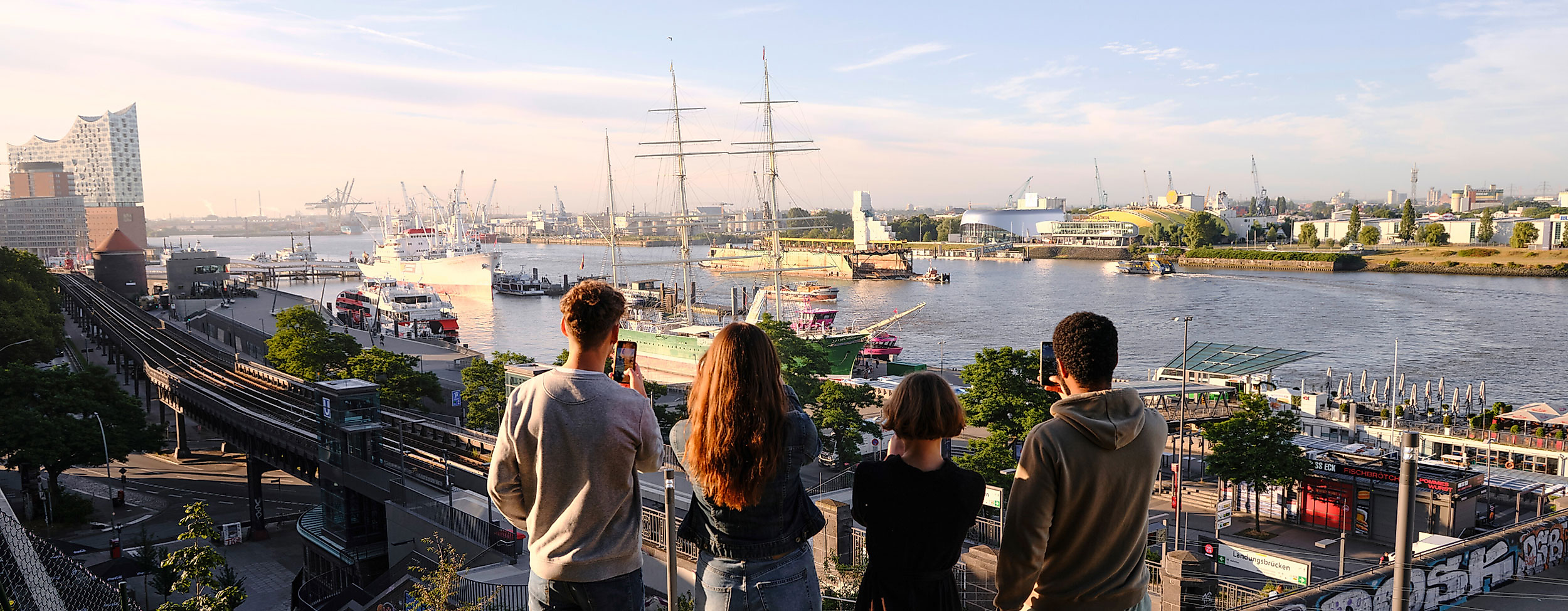 Vier Freunde schauen auf den Hamburger Hafen bei Sonnenaufgang vom Stintfang aus