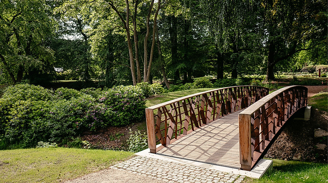 Holzbrücke auf dem Ohlsdorfer Friedhof Hamburg, umgeben von Bäumen und gepflegtem Grün.