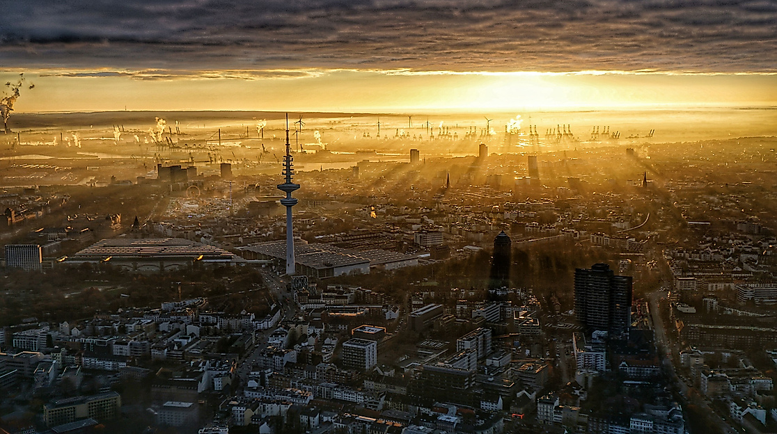 Luftaufnahme von Hamburg bei Sonnenaufgang mit Fernsehturm und Hafen im Gegenlicht.