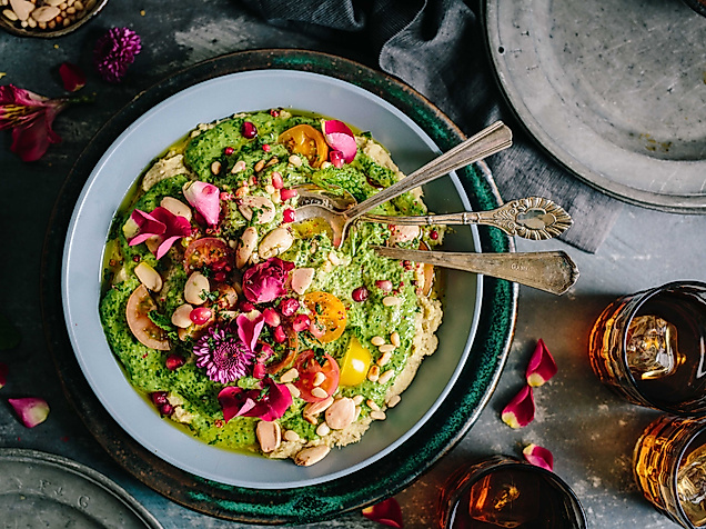 Farbenfrohe vegetarische Bowl mit Gemüse, Kräutern und essbaren Blüten, stilvoll angerichtet mit Besteck.