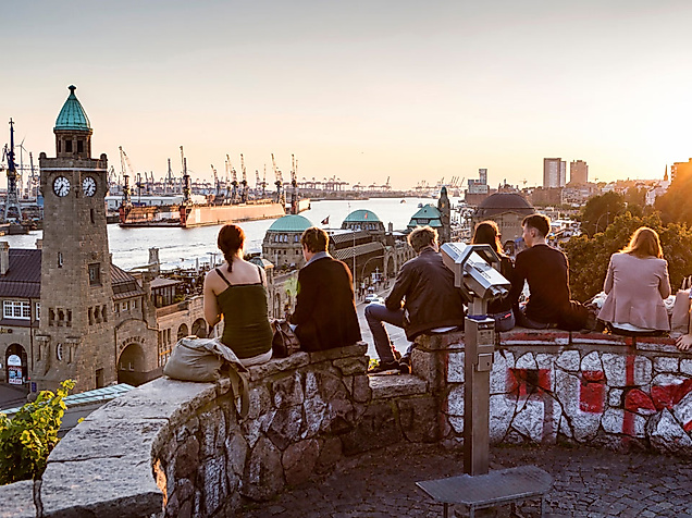 People enjoying the sunset with a view of Hamburg’s Landungsbrücken and the harbor in the background.
