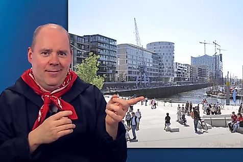 Mann gebärdet vor sonniger Promenade in der Hamburger HafenCity – barrierefreie Infos zum modernen Stadtteil.