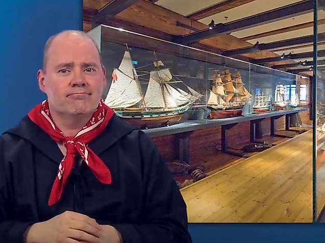 Mann gebärdet vor Ausstellungsraum mit maritimen Objekten – barrierefreie Infos zu Kultur in Hamburg.