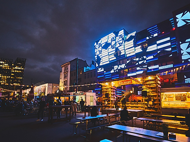 Spielbudenplatz bei Nacht mit beleuchteten Fassaden, Food-Ständen und leuchtender Straßenkunst in Blau und Gelb