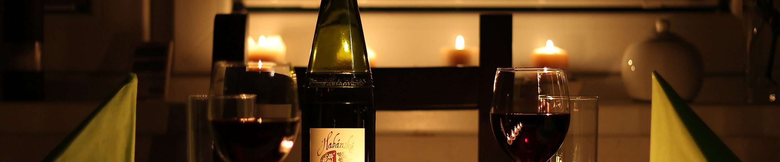 Romantisch gedeckter Tisch mit Kerzenlicht, Rotwein und Weinflasche für ein Candle-Light-Dinner