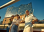 Three people on a boat in front of the Elbphilharmonie concert hall.