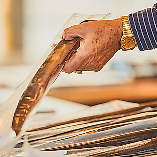 Hand hält geräucherten Aal auf dem Hamburger Fischmarkt über einem Tresen mit weiteren Fischen