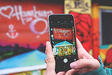 Smartphone fotografiert buntes Hamburg-Graffiti, Symbol für Social Media und Influencer-Kommunikation