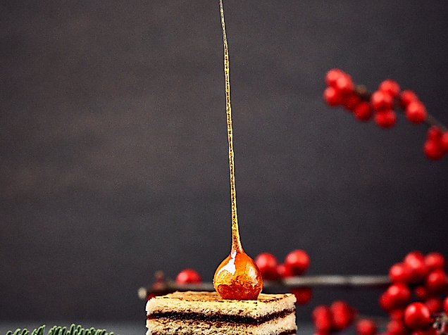 Festlicher Wintercake mit Karamellspitze auf Holzbrett, dekoriert mit Tannenzweigen und roten Beeren