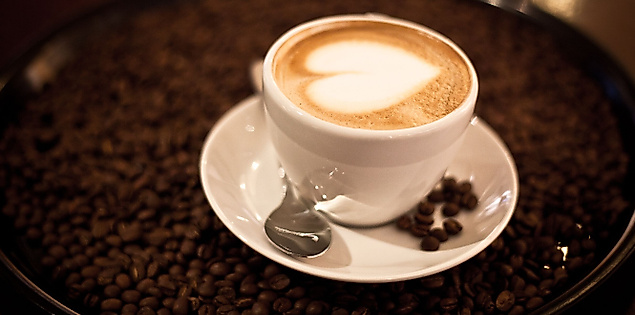 Cappuccino mit Herzlatte-Art in weißer Tasse auf Unterteller, serviert auf Kaffeebohnen